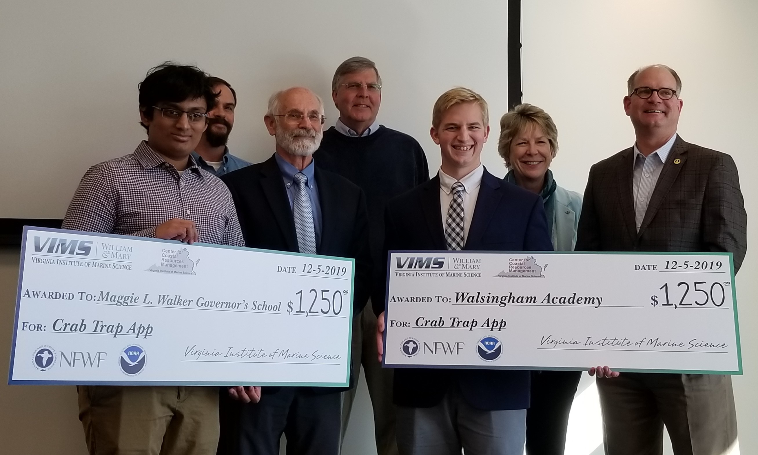 Group of people holding two oversized checks for $1,250 awarded December 5, 2019 to Maggie L. Walker Governor’s School and Walsingham Academy for the Crab Trap App.