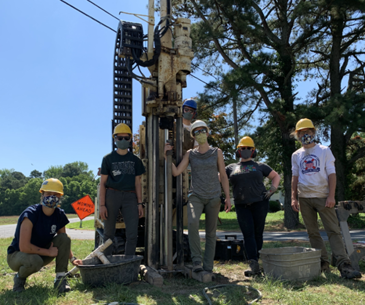 Coastal Geology Lab field crew stand in front of Geoprobe rill rig wearing COVID-19 masks