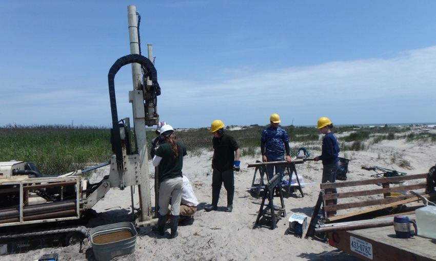 Group of lab members stand around Geoprobe drill rig during sample collection on the beach at Parramore Island, Virginia.