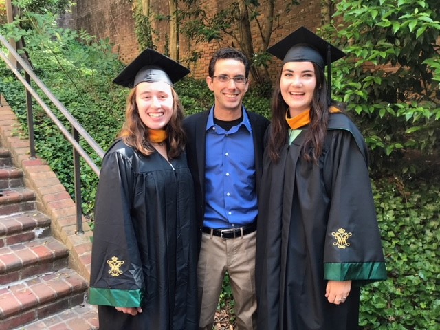 Chris Hein smiles with two students in graduation gowns