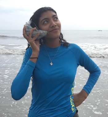 Coastal Geology Lab REU student Soely Luyando-Flusa poses with a large seashell held up to her ear like a phone